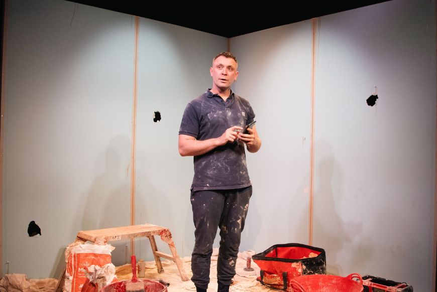 Mna standing on a stage, with lots of construction mess around him
