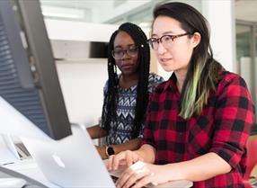 Bristol Internships - Woman working on computer with person standing behing her helping.