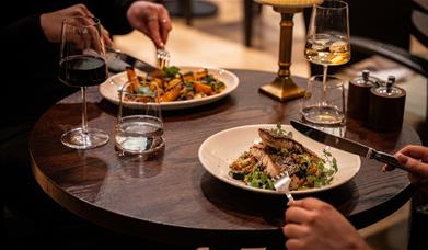 People using knife and fork to eat various dishes. One is fish on a bed of greens, and the other is unclear
