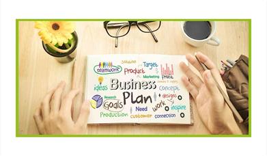 Stock photo of items on a table like someone's hands, glasses, and a page called Business Plan
