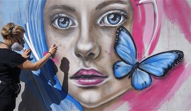 Person spraying mural of girl's face with butterfly