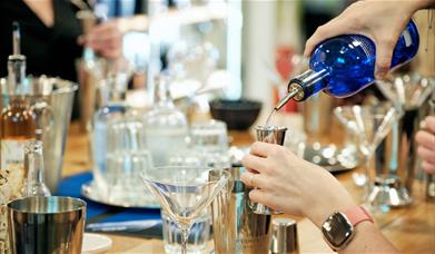 Person pouring gin and making a cocktail