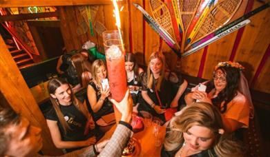 People around a table styled like a swiss chalet celebrating and being served food and drink