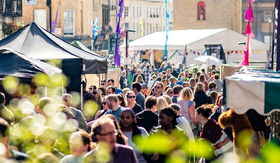 A crowd of people walking down Milsom Street, Bath, lined with food stands