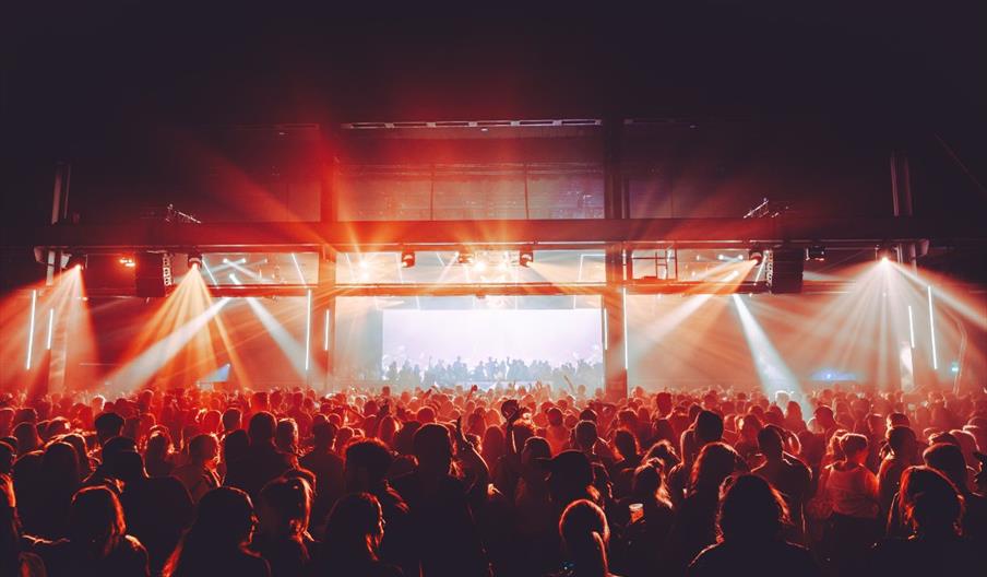 A live music event with a large crowd under red lighting