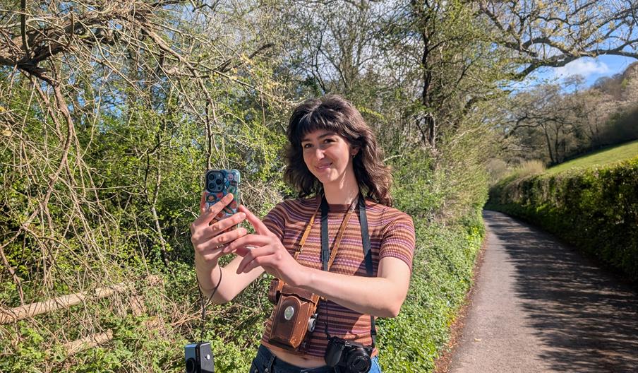 Person taking a photo with a phone with multiple other cameras around their neck and arm.