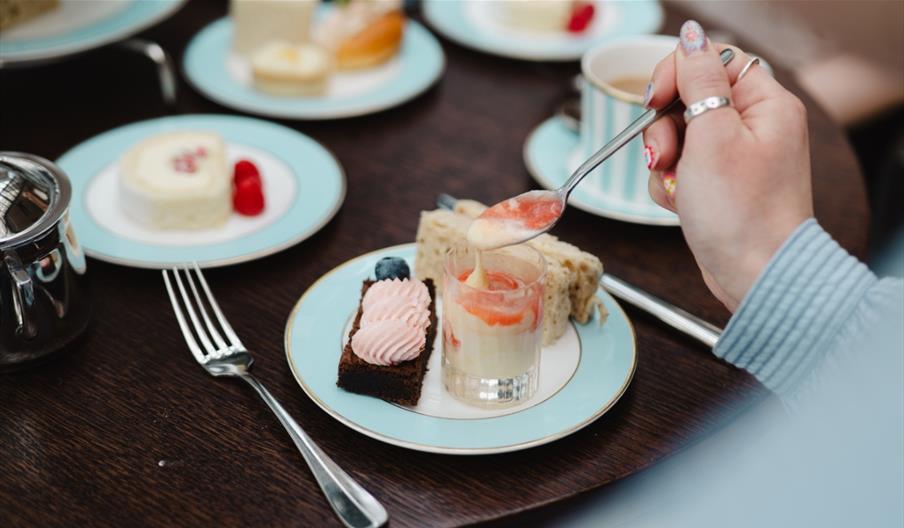 Person enjoying pastries, sandwich, and tea