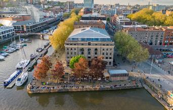 Aerial shot of the Arnolfini exterior, presumably via drone, showing its scenic location right on the harbourside. The shot is head-on and angled down