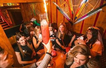 People around a table styled like a swiss chalet celebrating and being served food and drink