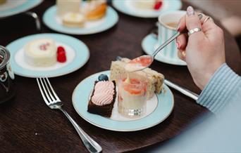 Person enjoying pastries, sandwich, and tea