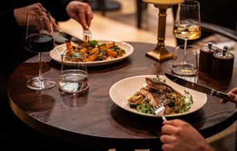 People using knife and fork to eat various dishes. One is fish on a bed of greens, and the other is unclear