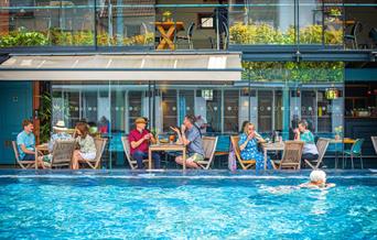 Bristol Lido - person swimming in pool and people dining by restaurant
