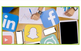 Photo from above a table looking down of phones, pens, tablets, hands, graphcs, and social media platform logos