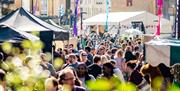 A crowd of people walking down Milsom Street, Bath, lined with food stands