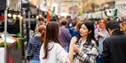 Two women standing in the middle of Milsom Street, Bath, lined with food and drink stands