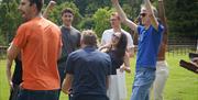 A group of adults outdoors laughing and celebrating in the summer with arms in the air.