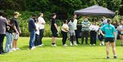 A group of adults in a row listening to an instructor outdoors on some grass as part of a team building exercise.