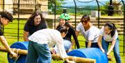 A group of adults laughing and making a raft from plastic barrels and wooden beams.