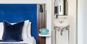 A bed with blue cushion and headboard, and a blue phone alongside. Open door to ensuite can be seen on the right.