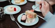 Person enjoying pastries, sandwich, and tea