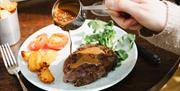 Hand drizzling sauce on a steak frites with a side salad