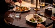 People using knife and fork to eat various dishes. One is fish on a bed of greens, and the other is unclear