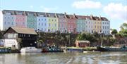 A row of multicoloured terraced houses overlooking boats on Bristol Harbour.