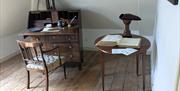 The interior of what may have been a study, with a chest of drawers extended and laid out like a work table, and a circular side table beside it with