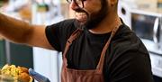 A man smiling and serving hummus and salad in a box