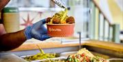 Someone serving falafel and salad in a take away bowl.