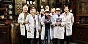 A group of people in white overcoats posing with their completion certificates, having completed the challenge. They are standing in front of a wall o