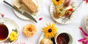 A birds-eye view of multiple plates holding tea, scones and other food items, with flowers scattered throughout