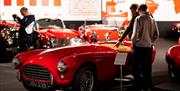 Two men looking into an open top small orange vintage car.
