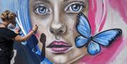 Person spraying mural of girl's face with butterfly