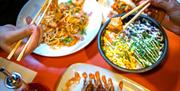 Noodle dishes, riche dishes, and hands holding chopsticks full of food.