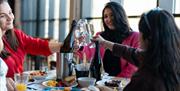 Three ladies sitting around a table having brunch with prosecco, toasting each other