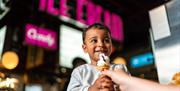 A small child looking very happy holding an ice cream with blurred pink neon lights in the background