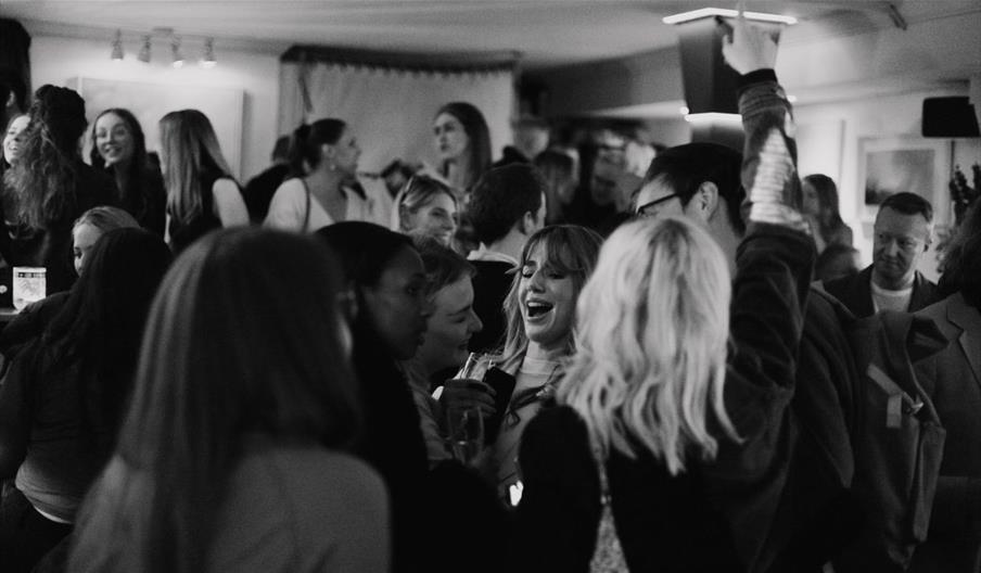 A black and white image of a room full of people, laughing and talking. A black and white image of a room full of people, laughing and talking.