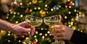Two people clinking glasses of wine in front of a Christmas tree