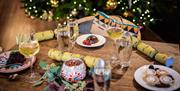 Image of a table set for a Christmas meal, with glasses of wine, crackers, mince pies, and other plates of food