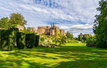 A view of green gardens with trees and box hedges with Berkeley Castle in the background