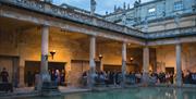 People gathered by great bath in Roman Baths at dusk
